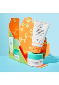 Two skincare products in a brightly patterned orange and green box: a white tube with an orange cap and a white jar with a turquoise lid.