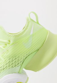 Lime vihreä urheilukenkä, jossa on tekstuuripintainen verkkoyläosa, valkoiset yksityiskohdat ja paksu pohja. Varustettu kätevällä vetotapilla kantapäässä helppoa pukemista varten.