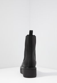 Černá kotníková bota s elastickými bočními panely, hladkým koženým svrškem, zaoblenou špičkou a robustní platformovou podrážkou. Minimalistický design bez ozdob.