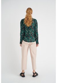 Blusa a fiori nera e verde con maniche lunghe, abbinata a pantaloni rosa pallido a sigaretta e sandali neri. Vista posteriore mostrata.