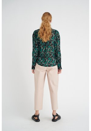 Blusa a fiori nera e verde con maniche lunghe, abbinata a pantaloni rosa pallido a sigaretta e sandali neri. Vista posteriore mostrata.