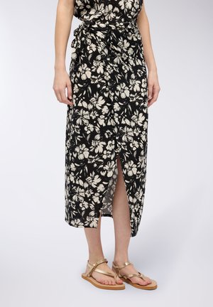 Vestito nero floreale con design avvolgente, caratterizzato da motivi di fiori bianchi e uno spacco laterale. Abbinato a sandali piatti dorati.
