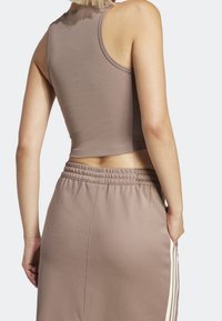 Brązowy, prążkowany crop top w połączeniu z beżowymi spodniami dresowymi z wiązaniem w pasie i białymi paskami po bokach. Gładka tkanina o luźnym kroju.