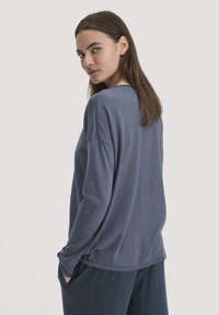 Blaues Langarmoberteil mit lockerer Passform und Rundhalsausschnitt, ausgestattet mit gerippten Bündchen und Saum. Kombiniert mit dunklen Hosen, glatte Stofftextur.