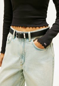 Top corto nero a costine con orlo a volant abbinato a jeans di denim azzurri a vita alta. Cintura in pelle nera con dettagli in fibbia argentata.