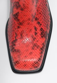 Stivale alla caviglia in stampa rettile rossa con finitura lucida, punta appuntita e un accento nero attorno alla suola. Misura circa 25 cm di lunghezza.