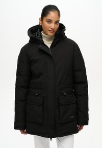Czarna ocieplana kurtka z kapturem, z wieloma przednimi kieszeniami i zamkami. Charakteryzuje się gładką fakturą oraz naszywką z logo na dolnej lewej stronie.