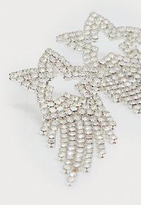 Zilveren stervormige oorbellen versierd met meerdere heldere rhinestones, met daaronder watervalletjes van rijtjes, in een glanzende metalen afwerking.