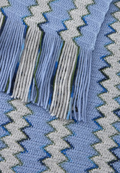 Tissu tricoté bleu et gris avec motif en zigzag et franges, montrant le détail du fil texturé et des nuances claires et foncées alternées.