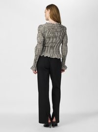 Tett, rutete overdelt med puffermer og volangnederkant, kombinert med svarte, rettbenede bukser med sideslits og stiletthæler.