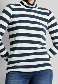 Haut col roulé avec des rayures horizontales bleu marine et blanches, en tissu doux. Manches longues et coupe ajustée. Accompagné de jeans en denim bleu.