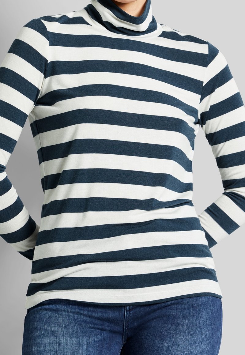 Haut col roulé avec des rayures horizontales bleu marine et blanches, en tissu doux. Manches longues et coupe ajustée. Accompagné de jeans en denim bleu.
