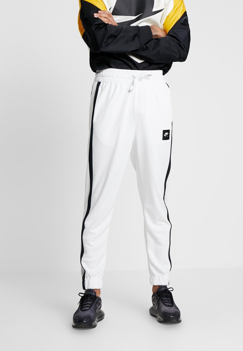 Vita idrottsbyxor med svarta sidostrecker, med elastisk midja och muddar, tillverkade av ett mjukt, lätt tyg.