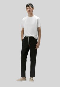 Witte T-shirt met korte mouwen en een reliëflogo, gecombineerd met zwarte broek met een trekkoord en tan schoenen met witte zolen.