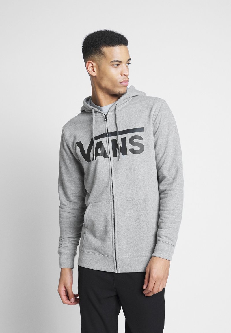 Szara bluza z kapturem na zamek błyskawiczny, z kieszenią typu kangur, z dużym czarnym logo "VANS" na klatce piersiowej oraz regulowanym kapturem. Wykonana z materiału bawełnianego.