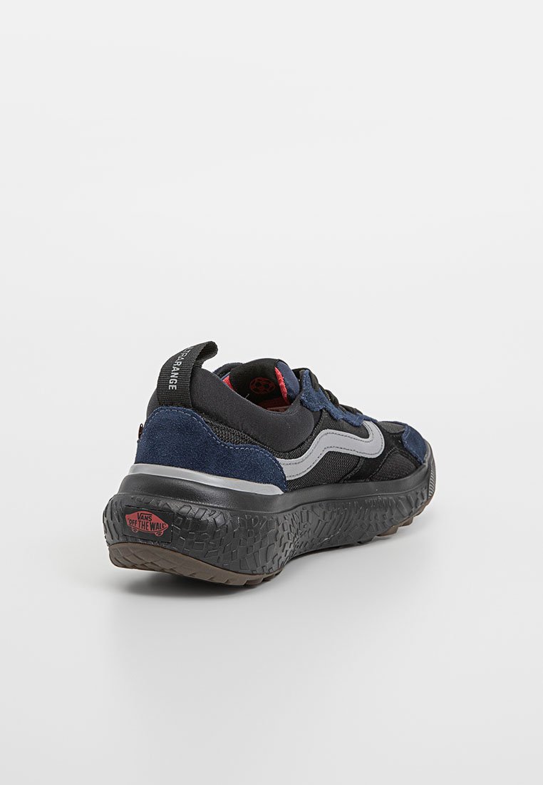 Zapatilla negra y azul marino con una suela de goma texturizada, parte superior de ante y malla, acentuada con detalles en gris claro y un interior rojo.