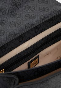 Käsin valmistettu musta laukku, jossa on kohokuvioitu malli, kultaiset metalliosat ja kankainen vuori, jossa on vetoketjullinen tasku ja bränditunnus.