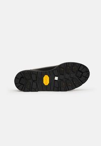 Suola di scarpa in gomma nera con un motivo di battistrada robusto e forme variabili, logo Vibram giallo e superficie texturizzata per una migliore aderenza.