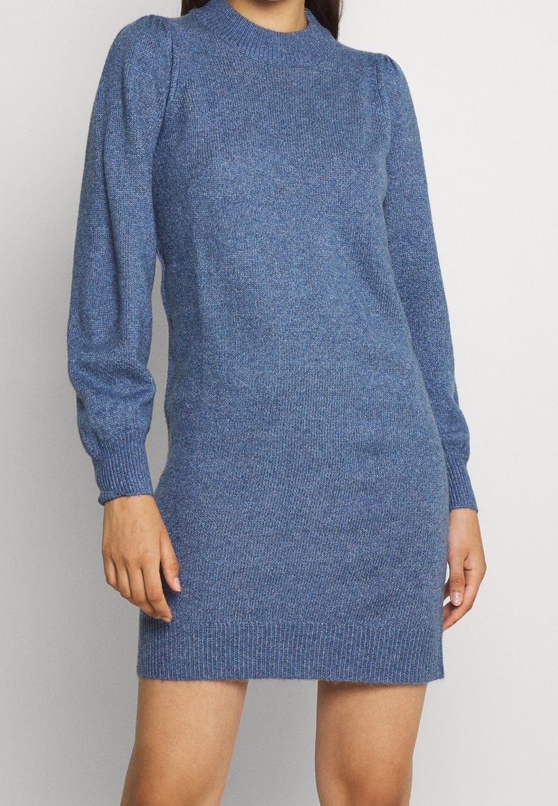 Abito azzurro lavorato a maglia con collo alto, maniche lunghe a sbuffo e polsi e orlo a coste. Texture morbida con sottili variazioni di colore.