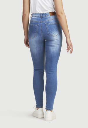 Höga blå jeans med en slät denimtextur, fem fickor och en brun läderetikett på bakre midjan. Accenterad med minimal blekning.