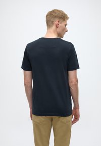T-shirt à col rond bleu marine foncé en coton, manches courtes, design uni, avec une petite étiquette au dos et une coupe décontractée, associé à un pantalon beige.