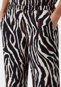 Schwarz-beige gestreifte Hose mit einem Zebra-Muster und bordeauxfarbenen Akzenten. Hergestellt aus einem strukturierten, leichten Stoff mit seitlichen Taschen.
