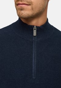 Marineblauer Strickpullover mit hohem Reißverschlusskragen. Verfügt über strukturierte Stoffe und einen silbernen Reißverschluss mit Branding. Enganliegendes Design.