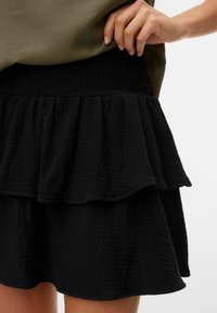 Jupe noire à volants avec un design texturé et froncé. Taille élastique pour un ajustement confortable. Le tissu semble léger et doux.