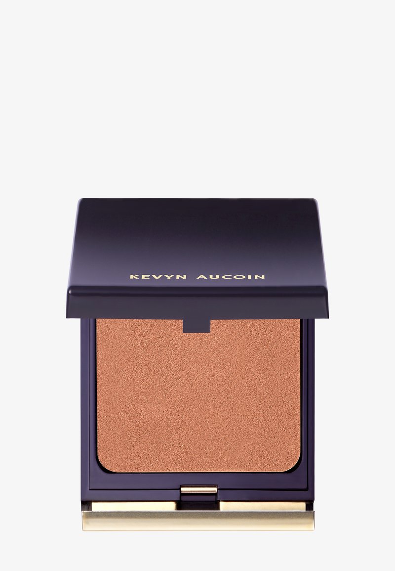 Geperst poeder bronzer in een vierkante paarse compact met een gouden accent. Gladde, matte afwerking in een warme, lichtbruine tint.