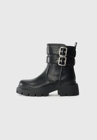 Black leather ankle boot with chunky sole and two silver buckle straps on the side, isolated on a light background.
