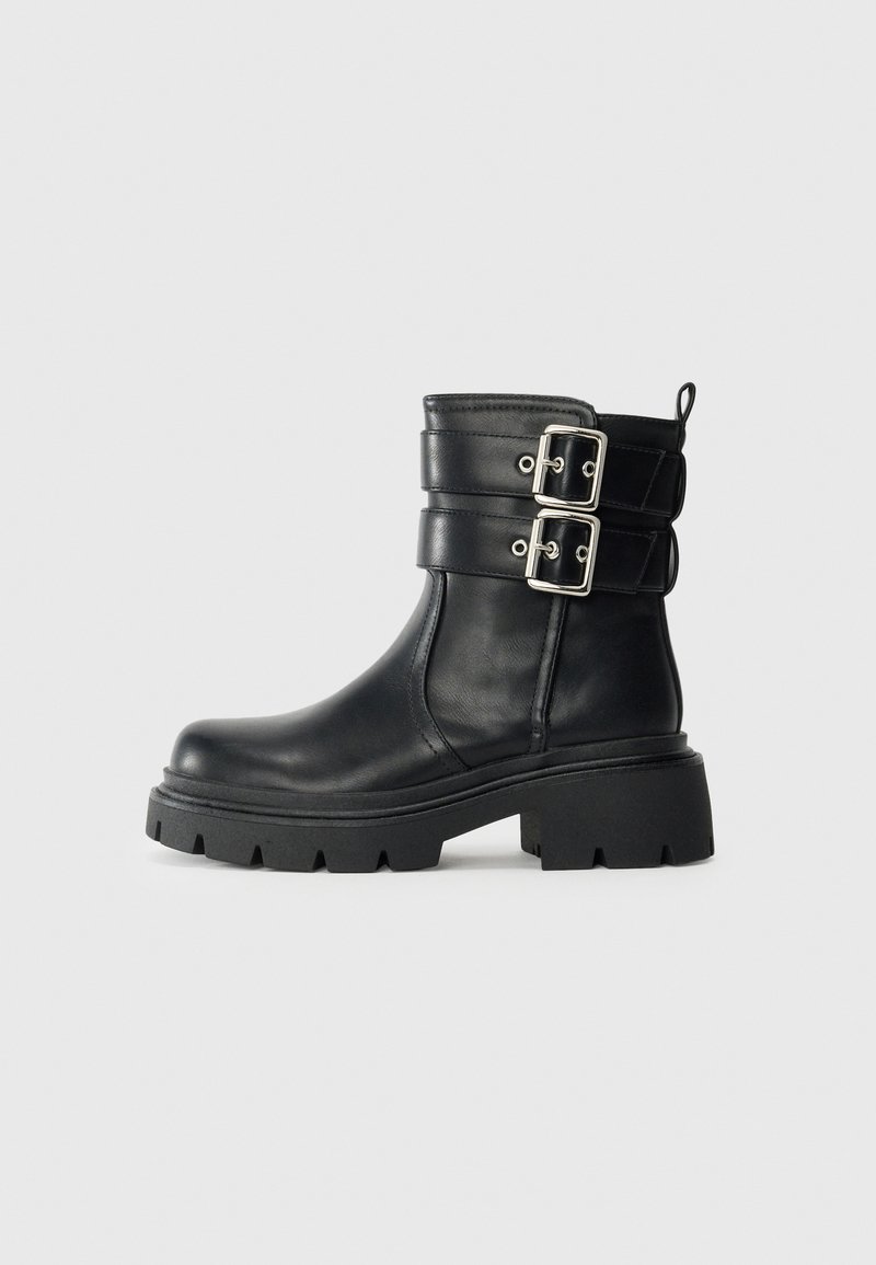 Black leather ankle boot with chunky sole and two silver buckle straps on the side, isolated on a light background.