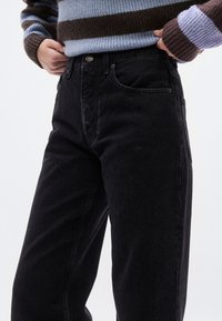 Μαύρο τζιν παντελόνι με ψηλή μέση και ίσια γραμμή. Διαθέτει εμπρόσθιες τσέπες και μεταλλικό κουμπί στο κλείσιμο. Ομαλή υφή και καλοσχηματισμένη εφαρμογή.