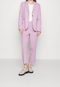 Svetle fialový oblekový blejzr s odpovídajícími zkrácenými kalhotami, s knoflíkovým zapínáním. Nosit s béžovými mokasíny a bílou blůzou s krajkovým vrškem.