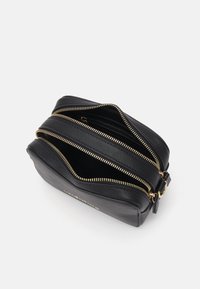 Sac en bandoulière en cuir noir avec deux zips, accessoires en or, texture lisse et forme rectangulaire compacte. Intérieur doublé.