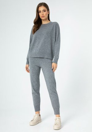 Grijze gebreide loungewear set bestaande uit een top met lange mouwen en aansluitende broek, vervaardigd uit zacht materiaal met geribbelde accenten bij de manchetten en de zoom.