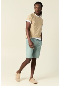 Camiseta beige de manga corta sobre una camisa blanca, combinada con pantalones cortos verde claro y zapatos de tela crema. Diseño simple y casual con acentos mínimos.