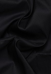 Il tessuto nero mostra una consistenza liscia e opaca con un leggero lucido. Il materiale è drappeggiato, evidenziando le sue morbide pieghe e il colore uniforme.