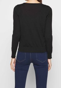 Svart långärmad tröja med rund halsringning och ribbat fåll. Bärs med mörkblå jeans som har bakfickor och lätt stretch.