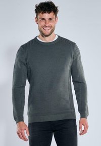 Grauer ribbeliger Strickpullover mit langen Ärmeln und rundem Halsausschnitt. Auffällige Texturen an den Schultern und Seiten.