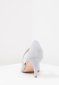 Grå mocka högklackad sko med spetsig tå och smal klack. Har en utskärning på sidan för extra detalj.