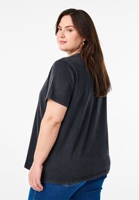 Camiseta negra de gran tamaño con mangas cortas, textura suave y cuello redondo. Presenta un ajuste holgado, que cae justo por debajo de las caderas.
