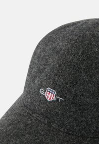 Gorra de béisbol de fieltro gris oscuro con un logotipo bordado y acentos rojos y azules en el lateral. Textura suave con forma estructurada.