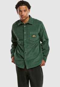 Grønn kordfløyelskjorte med lange ermer, knapp foran og lomme med brodert "Obey"-logo. Strukturert overflate og normal passform.