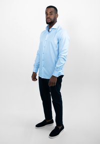 Lichtblauwe lange mouwen shirt met knoopdetails, slim fit en zachte stof; gecombineerd met donkere broeken en zwarte instappers.