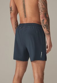 Costume da bagno corto blu navy realizzato in tessuto leggero, con vita elasticizzata e spacchi laterali per una maggiore mobilità. Include una tasca posteriore con zip.