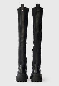 Botas pretas até ao joelho, apresentando uma mistura de tecido texturizado e couro liso, com detalhes de marcação verticais e solas de borracha grossa.