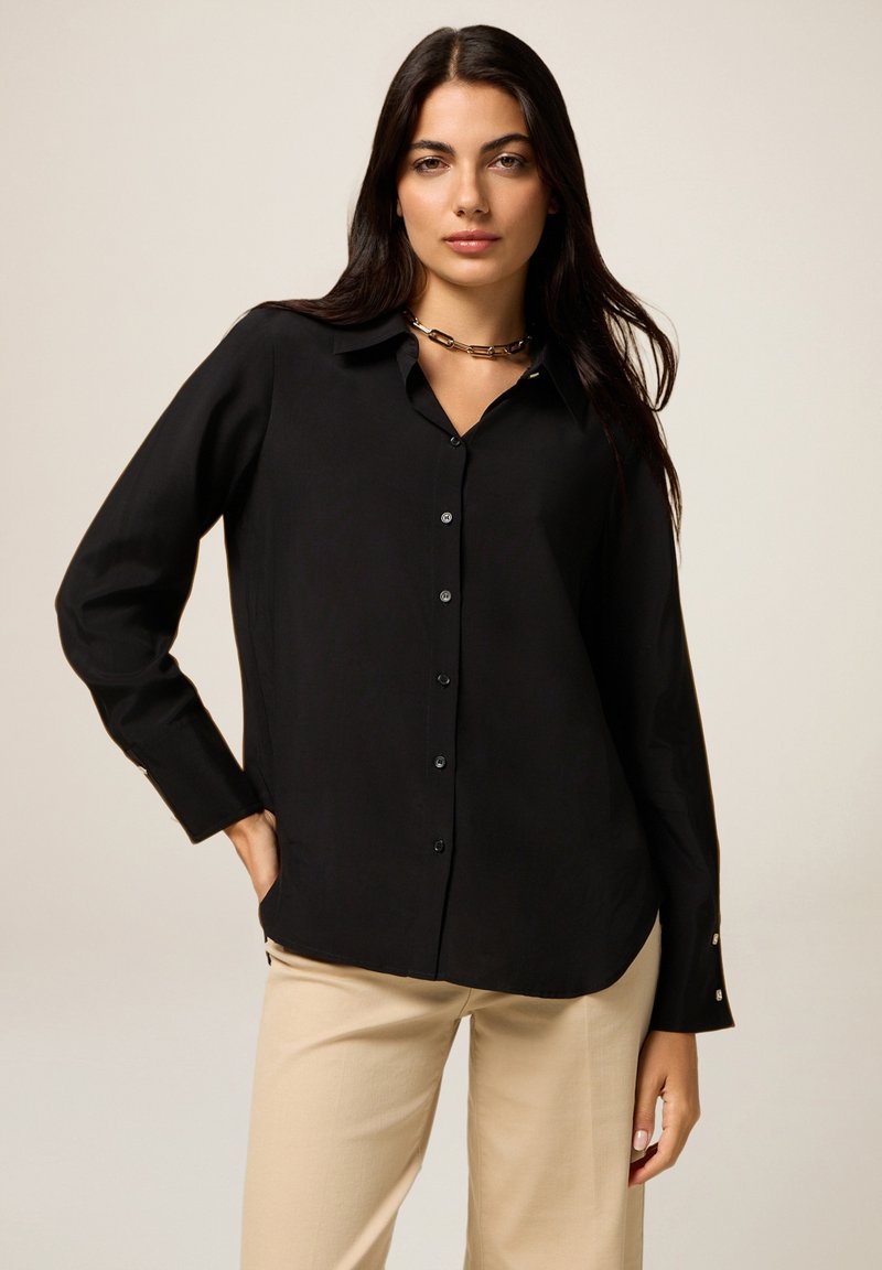 Black button-up shirt made of smooth fabric, featuring long sleeves and a classic collar. Accented with small buttons at the cuffs.