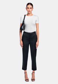 Witte aansluitende top met korte mouwen, gecombineerd met hoge zwarte pantalon. Model houdt een zwarte handtas vast en draagt zwarte sandaaltjes met bandjes.