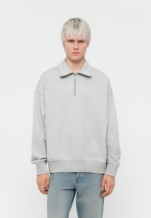Light gray sweatshirt with a high collar and a quarter-zip front. Features dropped shoulders and a relaxed fit, made of soft fabric.