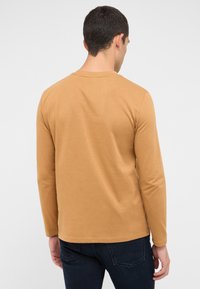 Langarmhemd in warmem Tan-Ton aus weichem Stoff, mit Rundhalsausschnitt, geradem Saum und eng anliegenden Ärmeln. Minimalistisches Design.